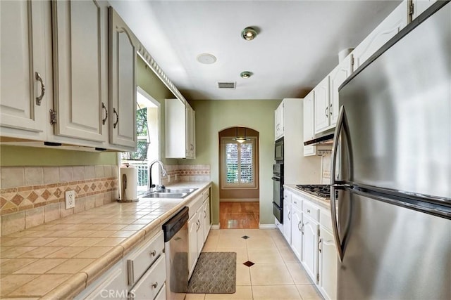 kitchen with a sink, visible vents, black appliances, tile countertops, and light tile patterned flooring