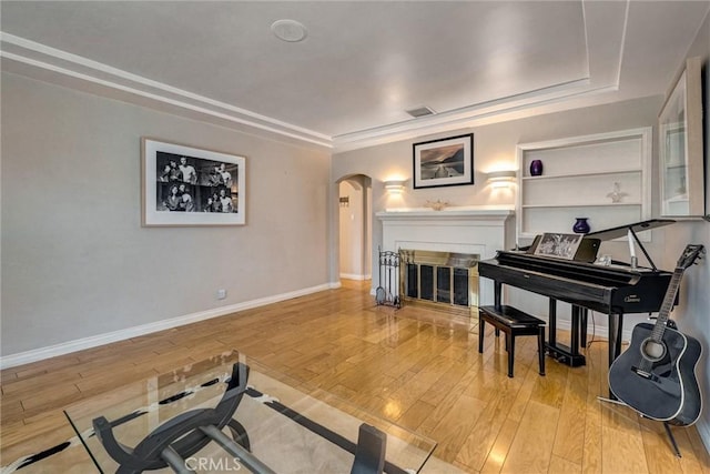 sitting room featuring hardwood / wood-style floors, visible vents, arched walkways, baseboards, and a fireplace with flush hearth