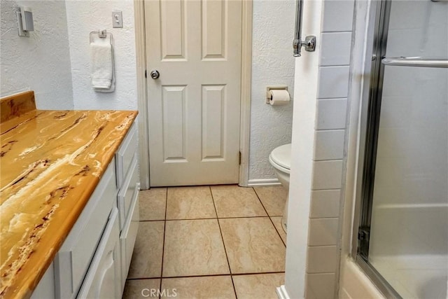 bathroom featuring a shower with shower door, toilet, vanity, tile patterned floors, and a textured wall