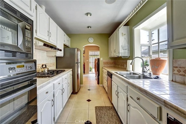 kitchen with tile countertops, a sink, white cabinetry, arched walkways, and black appliances