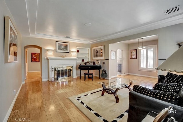 living room featuring wood-type flooring, visible vents, arched walkways, and a glass covered fireplace