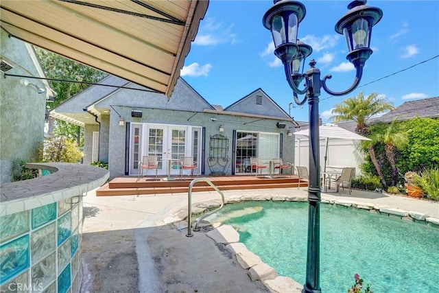 rear view of property with french doors, fence, a patio, an outdoor pool, and stucco siding
