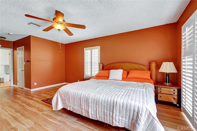 bedroom featuring baseboards, visible vents, a textured ceiling, and wood finished floors
