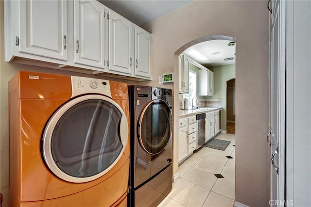 clothes washing area with independent washer and dryer, light tile patterned floors, a sink, arched walkways, and cabinet space