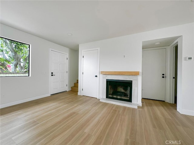unfurnished living room with a premium fireplace, light wood finished floors, baseboards, and stairway