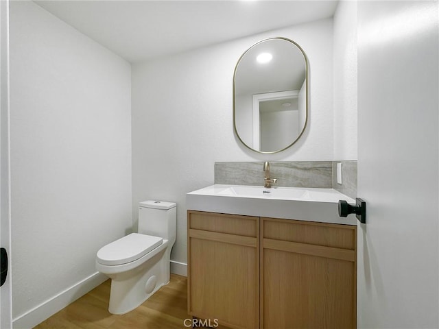 half bathroom with toilet, baseboards, vanity, and wood finished floors