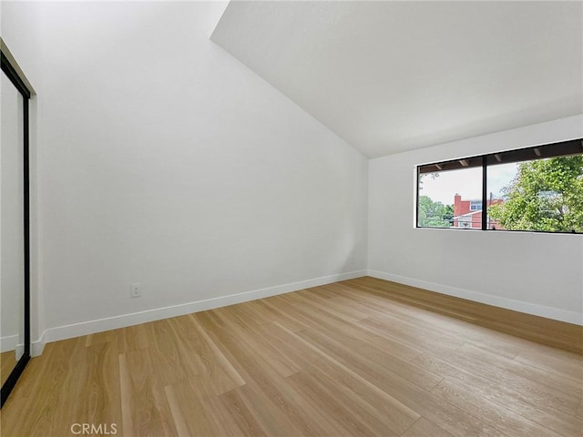 spare room featuring baseboards, light wood-type flooring, and vaulted ceiling