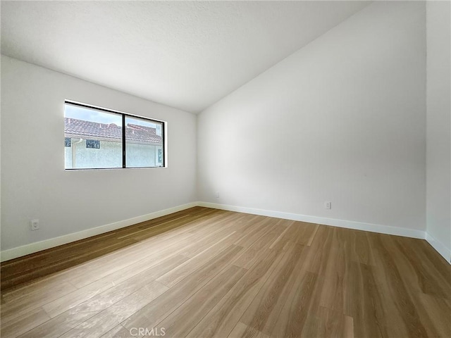 unfurnished room with vaulted ceiling, wood finished floors, and baseboards
