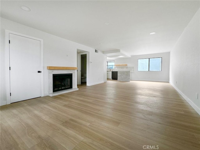 unfurnished living room featuring light wood finished floors, baseboards, a fireplace with raised hearth, and visible vents