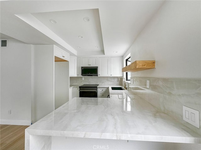 kitchen featuring a sink, a peninsula, stainless steel appliances, light stone counters, and backsplash
