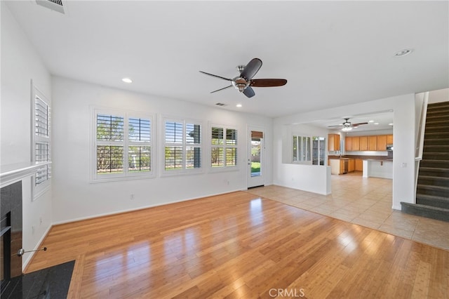 unfurnished living room featuring a ceiling fan, stairs, a tile fireplace, and plenty of natural light