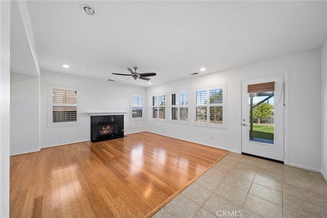unfurnished living room featuring a premium fireplace, a ceiling fan, a healthy amount of sunlight, and recessed lighting