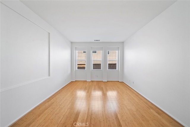 spare room featuring light wood-style floors, visible vents, and baseboards