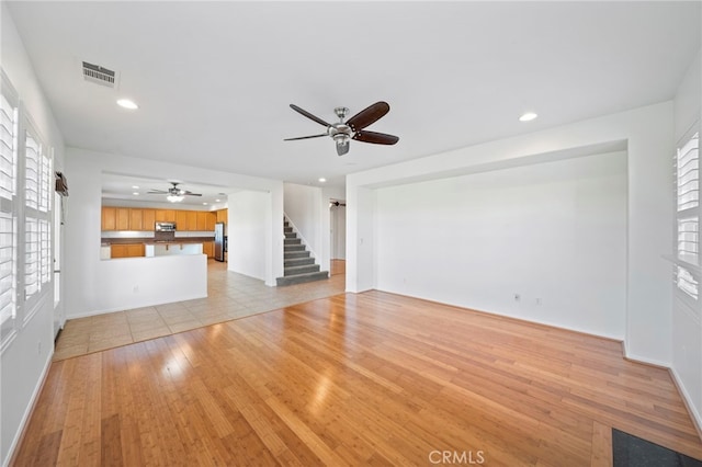 unfurnished living room with a ceiling fan, recessed lighting, baseboards, visible vents, and stairway