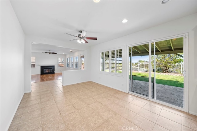 unfurnished living room with baseboards, a glass covered fireplace, and ceiling fan