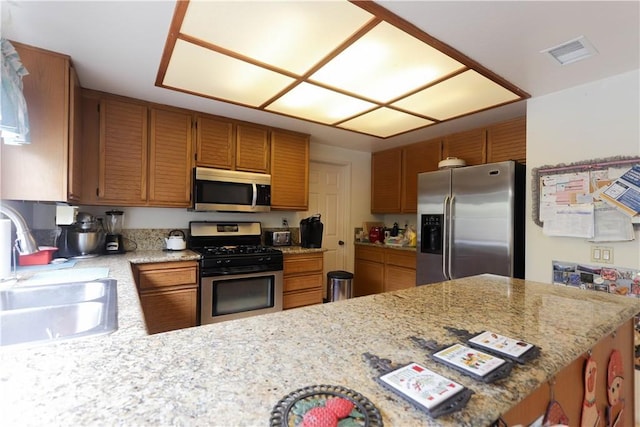 12592 Arlington Pl, Chino, CA 91710 - kitchen featuring stainless steel appliances, a sink, brown cabinetry, a peninsula, and light stone counters