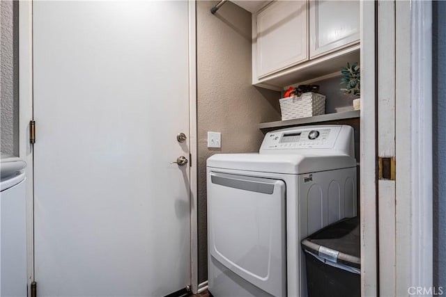 clothes washing area featuring cabinet space, washing machine and dryer, and a textured wall