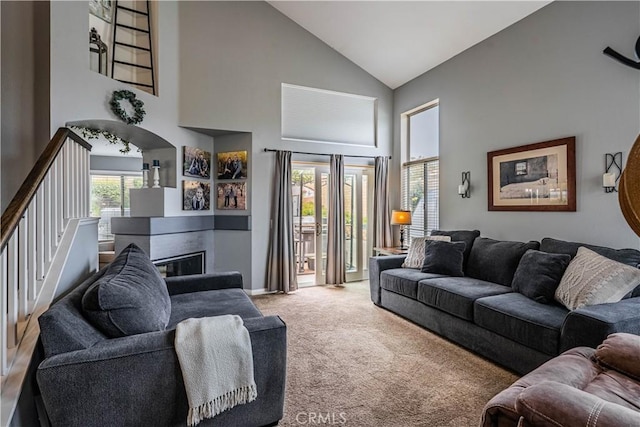 carpeted living area featuring stairway, high vaulted ceiling, and a glass covered fireplace