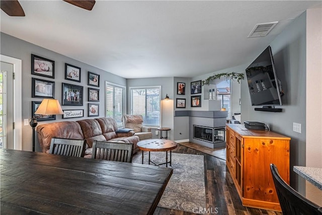 living area with a ceiling fan, baseboards, dark wood finished floors, visible vents, and a fireplace