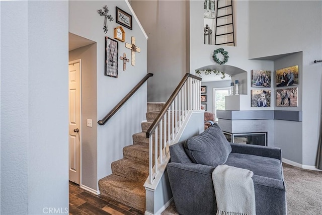stairway featuring a fireplace, a towering ceiling, baseboards, and wood finished floors