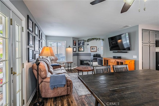 living area with visible vents, dark wood-style flooring, ceiling fan, and a glass covered fireplace