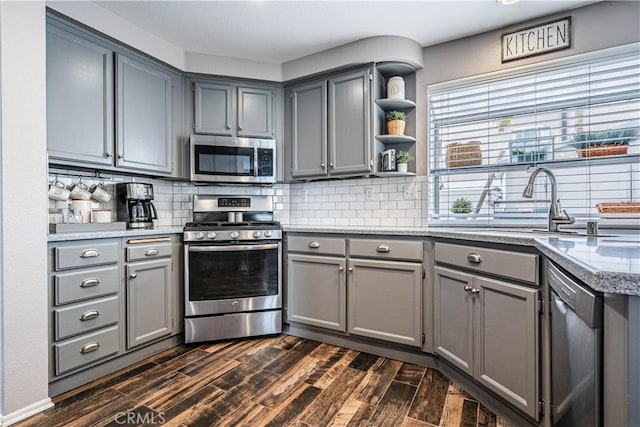 kitchen with gray cabinetry, dark wood finished floors, a sink, open shelves, and appliances with stainless steel finishes