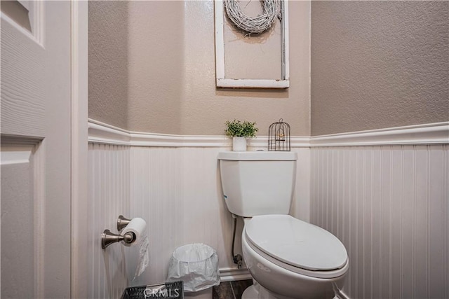 half bath with toilet, wainscoting, and a textured wall