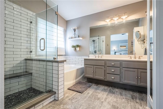 full bath featuring a bath, a sink, a shower stall, double vanity, and wood finished floors