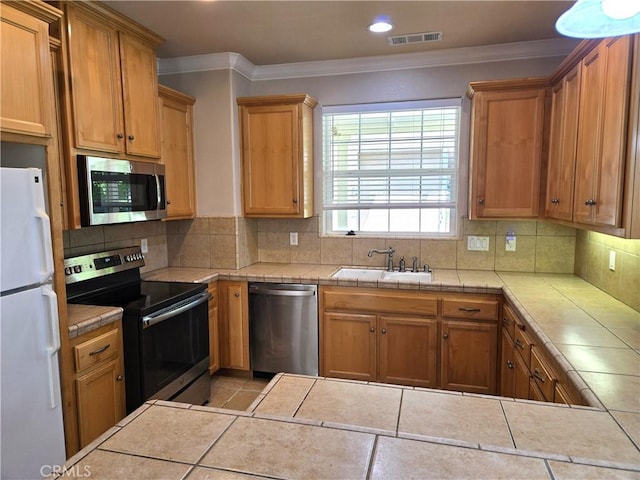 kitchen with stainless steel appliances, tile counters, ornamental molding, and a sink