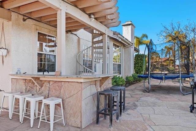 view of patio featuring stairs, a trampoline, and outdoor dry bar