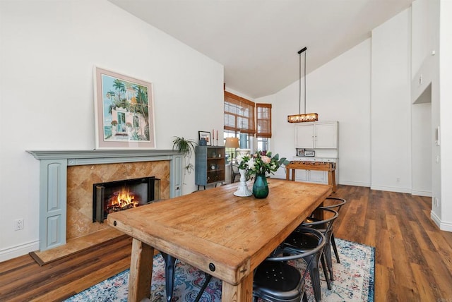 dining area featuring dark wood finished floors, high vaulted ceiling, baseboards, and a high end fireplace