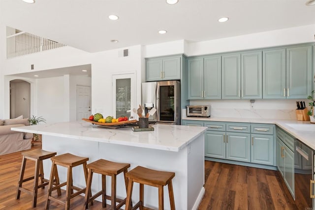 kitchen featuring light stone counters, a breakfast bar area, recessed lighting, dark wood finished floors, and stainless steel fridge