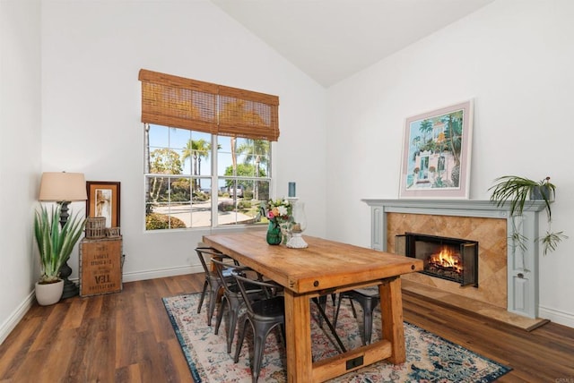 dining room with high vaulted ceiling, baseboards, a high end fireplace, and wood finished floors
