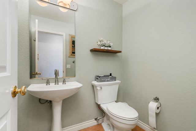 half bathroom with toilet, baseboards, and a sink