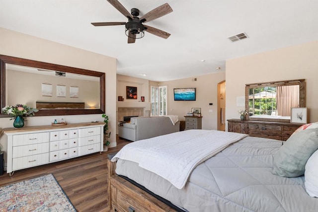 bedroom featuring a fireplace, dark wood-style flooring, ceiling fan, and visible vents
