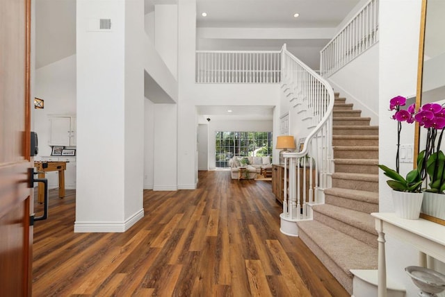 foyer entrance featuring baseboards, wood finished floors, a towering ceiling, and stairs