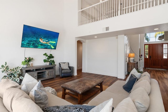 living area with wood finished floors, a high ceiling, visible vents, baseboards, and arched walkways