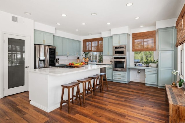 kitchen with recessed lighting, appliances with stainless steel finishes, dark wood-style floors, and a breakfast bar
