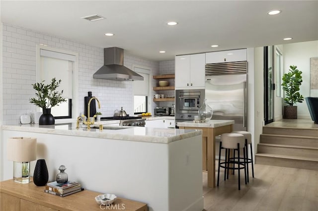 kitchen with open shelves, visible vents, wall chimney exhaust hood, light wood-style flooring, and white cabinetry