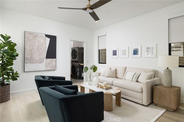 living room featuring a ceiling fan, stacked washer and dryer, light wood-style flooring, and baseboards