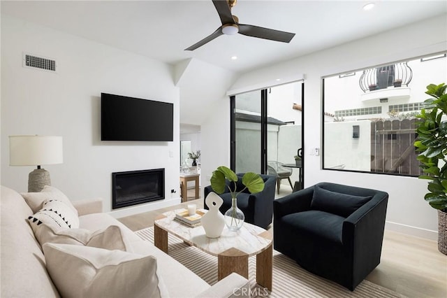 living area featuring a healthy amount of sunlight, a glass covered fireplace, visible vents, and wood finished floors