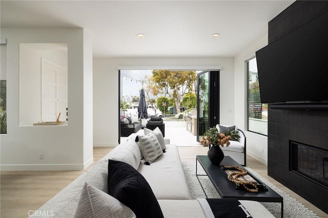 living room featuring recessed lighting, a tile fireplace, baseboards, and light wood-style floors