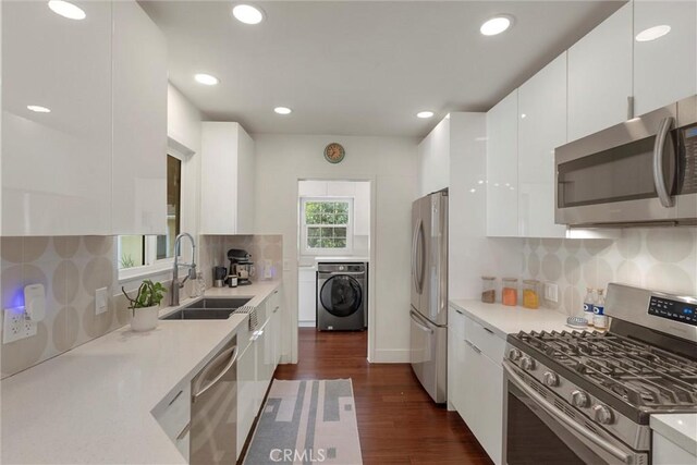kitchen with a sink, stainless steel appliances, washer / dryer, white cabinetry, and light countertops