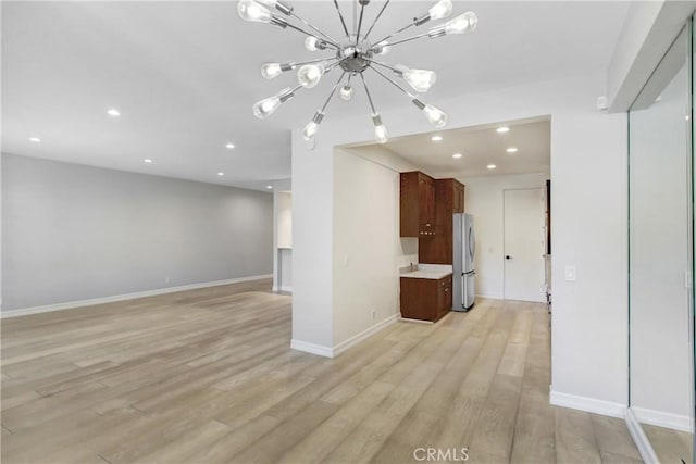 unfurnished living room with light wood finished floors, an inviting chandelier, baseboards, and recessed lighting