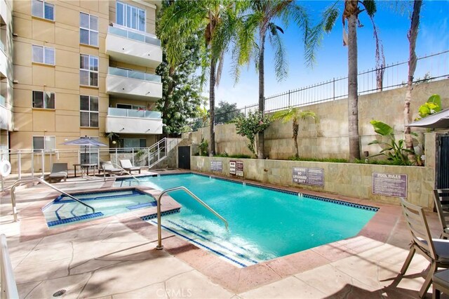 community pool with a patio, a hot tub, and fence