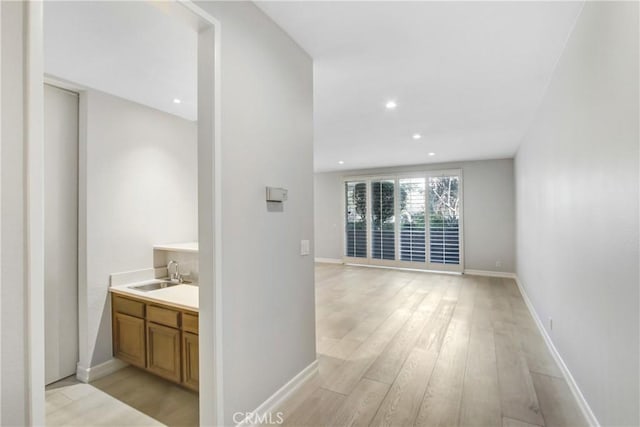 corridor with baseboards, light wood-style flooring, recessed lighting, and a sink