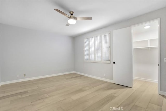 unfurnished bedroom featuring a ceiling fan, a closet, baseboards, a spacious closet, and light wood-style floors