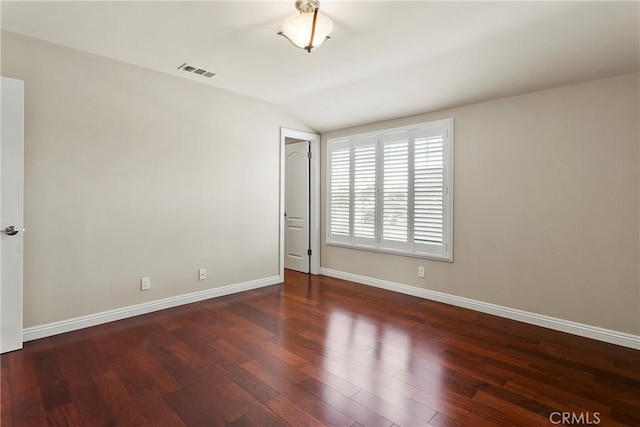empty room featuring vaulted ceiling, visible vents, wood finished floors, and baseboards