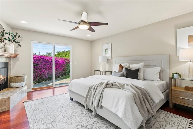 bedroom with a ceiling fan, recessed lighting, a tiled fireplace, access to outside, and wood finished floors