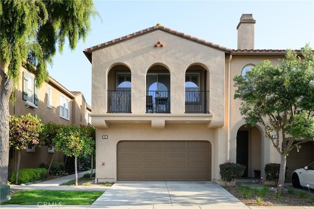 mediterranean / spanish-style house featuring a balcony, a chimney, driveway, a garage, and stucco siding